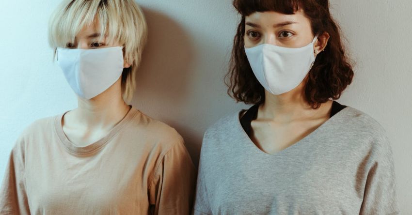Benefits - Asian women in home wear in medical masks attentively looking away while standing against white wall
